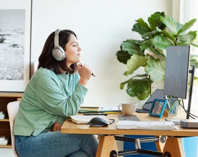 Kvinna med hörlurar som håller en penna och tittar på en datorskärm