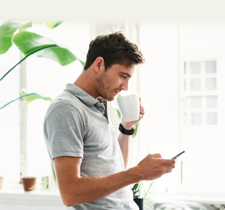 En man dricker kaffe med en mobiltelefon i handen