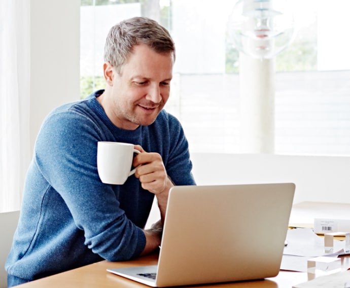 Man hemma som använder en bärbar dator och dricker kaffe.