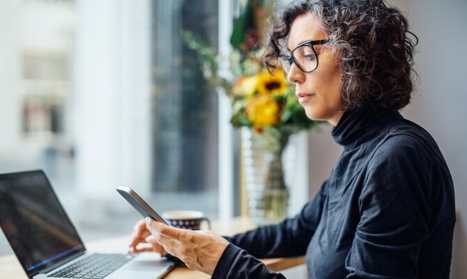 Kvinna som tittar på en mobiltelefon framför en laptop