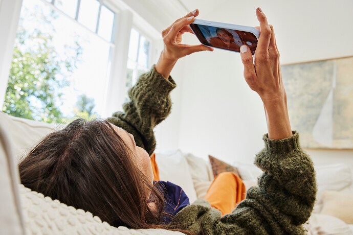 Kvinna som ligger ner och tittar på en mobiltelefon